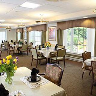 A well-appointed dining room with neatly arranged tables and chairs, featuring large windows and floral decorations.