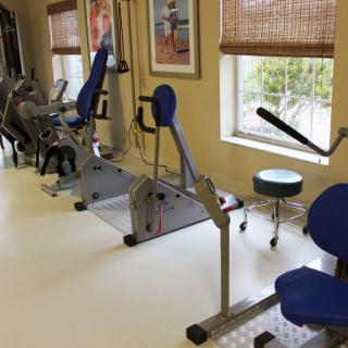 A fitness room with various exercise equipment lined up along the windows.