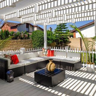 A modern outdoor patio with stylish seating under a pergola, featuring decorative pillows and vibrant sunlight.