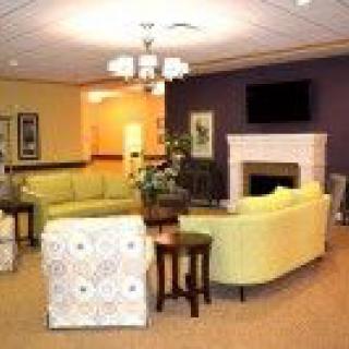 A cozy living room with light green sofas, a fireplace, and a TV on the wall.