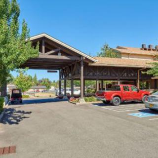 A building with a covered entrance and parked vehicles on a sunny day.