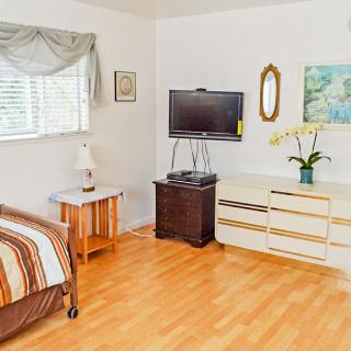 A cozy bedroom featuring a television, dresser, and window with natural light.