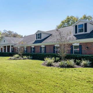 A large brick residential house with a well-maintained lawn and landscaped garden.