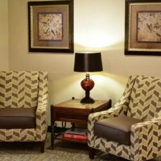 A cozy living room setup with patterned chairs, a wooden side table, a lamp, and framed artwork on the wall.
