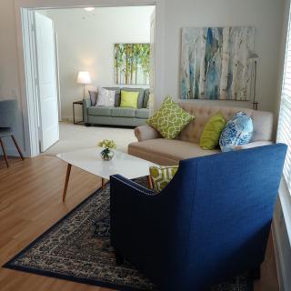 A cozy living room with modern furnishings, including a blue armchair, a beige sofa, and decorative cushions, complemented by abstract artwork and a coffee table.