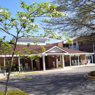A sunny day view of a building entrance with surrounding trees and driveway.