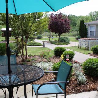 A serene patio setup with an umbrella and outdoor furniture overlooking a well-maintained garden and pathway.