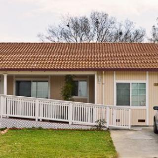 A single-story house with a tiled roof, featuring a ramp leading to the front entrance and a driveway alongside a green lawn.