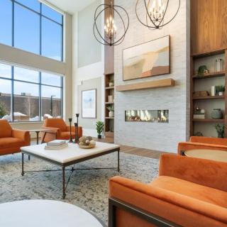 A modern living room with large windows, high ceilings, and orange chairs.