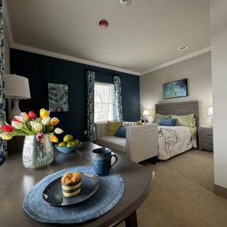 A cozy living space with a sofa, bed, and a table decorated with flowers and a cup.