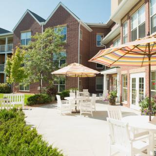 A sunny outdoor patio area with tables, chairs, and umbrellas in front of a building.