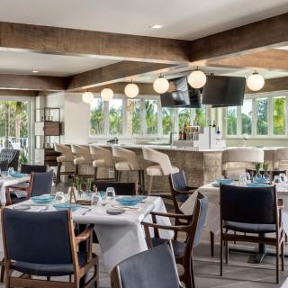 A modern restaurant interior with dining tables and a bar area featuring elegant lighting.