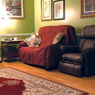 A cozy living room featuring a sofa with a red cover, a recliner chair, and decorative wall art on green walls.