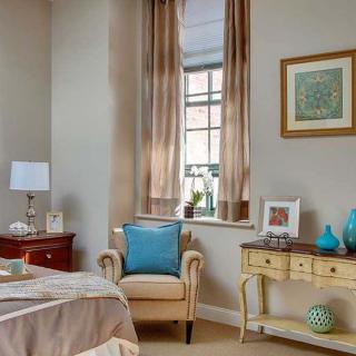 A cozy bedroom featuring an elegant armchair, soft curtains, and tasteful decor.