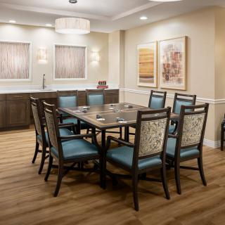 A modern dining room with a rectangular table and six upholstered chairs, featuring wall art and ambient lighting.