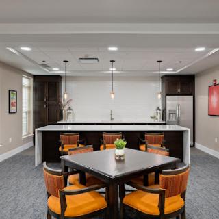 A modern kitchen-dining area featuring a stylish table and chairs with orange upholstery, illuminated by pendant lights.
