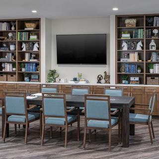 A modern conference room with a large table, chairs, and bookshelves.