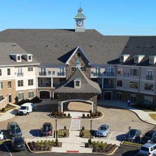An aerial view of a large residential building with a clock tower and an entrance surrounded by a parking lot.