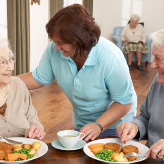 A caregiver assists elderly residents during mealtime in a nursing home.
