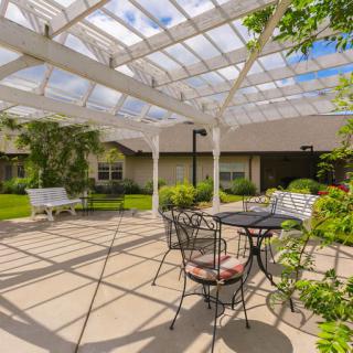 A sunny patio with metal furniture and a pergola surrounded by lush greenery.