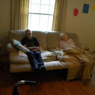 Two people resting on a sofa in a living room with sunlight coming through the window.