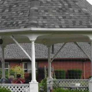 A garden gazebo with a shingled roof and surrounding greenery.