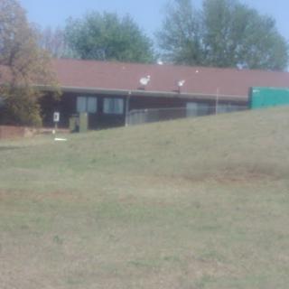 A view of a house situated on a grassy hill with trees in the background.
