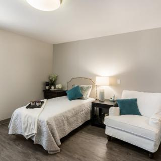 A cozy and elegantly designed bedroom with a single bed, comfortable chair, and stylish decor.
