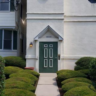 A building entrance with a green door and neatly trimmed shrubbery lining the pathway.