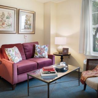A cozy living room with a red sofa, floral cushions, and a glass coffee table.