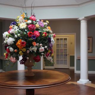A large and colorful flower arrangement on a wooden table in an elegant interior setting with columns.