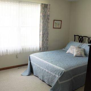 A simple bedroom with a blue bedspread and natural light coming through a window.