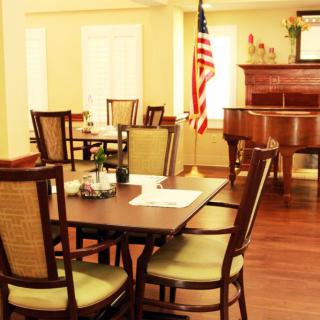 A cozy dining area with a wooden table and chairs, featuring a piano and an American flag in the background.