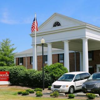 A library building with classical columns and a flagpole, featuring parked vehicles in the foreground.