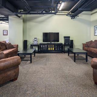 A cozy living room with brown sofas, a TV, and coffee tables on a carpeted floor.
