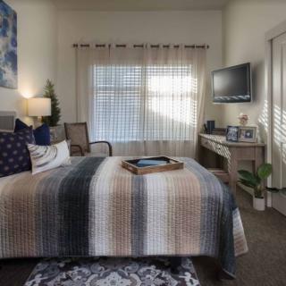 A cozy bedroom with a neatly made bed, television, and warm lighting.