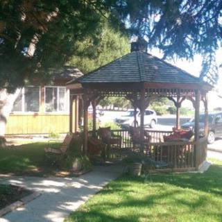 A wooden gazebo surrounded by a lush green lawn and trees, basking in sunlight.