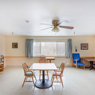 A bright and spacious dining area featuring a table with chairs, a ceiling fan, and large windows allowing natural light to fill the room.