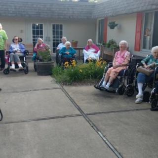 A group of seniors enjoying a social gathering outdoors in a garden area, with some seated in wheelchairs.