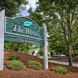 Entrance sign to The Woods community, surrounded by greenery and well-maintained landscaping.