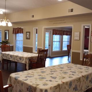 A cozy dining area with tables covered in floral-patterned tablecloths and surrounded by wooden chairs.