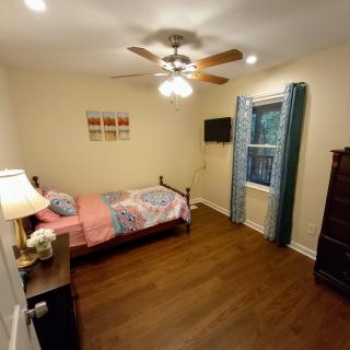 A cozy bedroom with a single bed, ceiling fan, and wooden flooring.