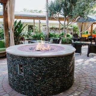 An inviting outdoor patio featuring a round fire pit surrounded by comfortable seating, set amidst lush greenery.