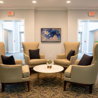 A cozy lobby seating area with four high-backed armchairs surrounding a round coffee table, adorned with decorative pillows and modern artwork on the wall.