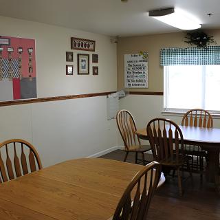 A cozy dining room with wooden chairs and tables, decorated with wall art and a window with a curtain.