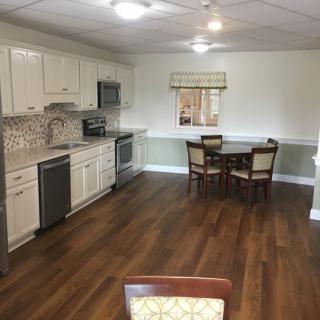 A spacious kitchen with wooden flooring, modern white cabinets, and a dining area with a table and chairs.