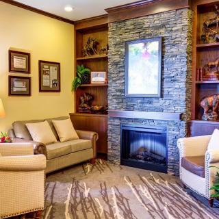 A cozy living room with a stone fireplace, comfortable seating, and decorative shelves.