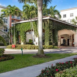 A building entrance adorned with ivy, surrounded by palm trees and well-maintained landscaping.