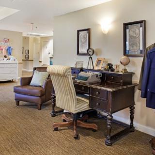 A cozy home office with a vintage wooden desk, an upholstered chair, and warm lighting.