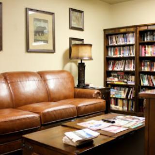 A cozy living room featuring a brown leather sofa, a wooden coffee table with magazines, and a bookshelf filled with various books.
